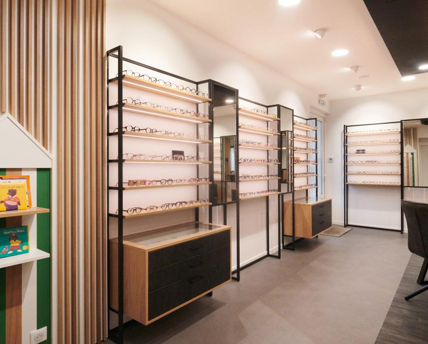 Repenser son agencement en diminuant son exposition tout en la mettant plus en valeur Et profiter de son extension pour accueillir au mieux ses clients Des mobiliers sur mesure bois/métal avec éclairage intégré Une salle d’examen de vue Un atelier ouvert sur l’espace de vente Un ilot de table de vente facilitant la circulation périphérique