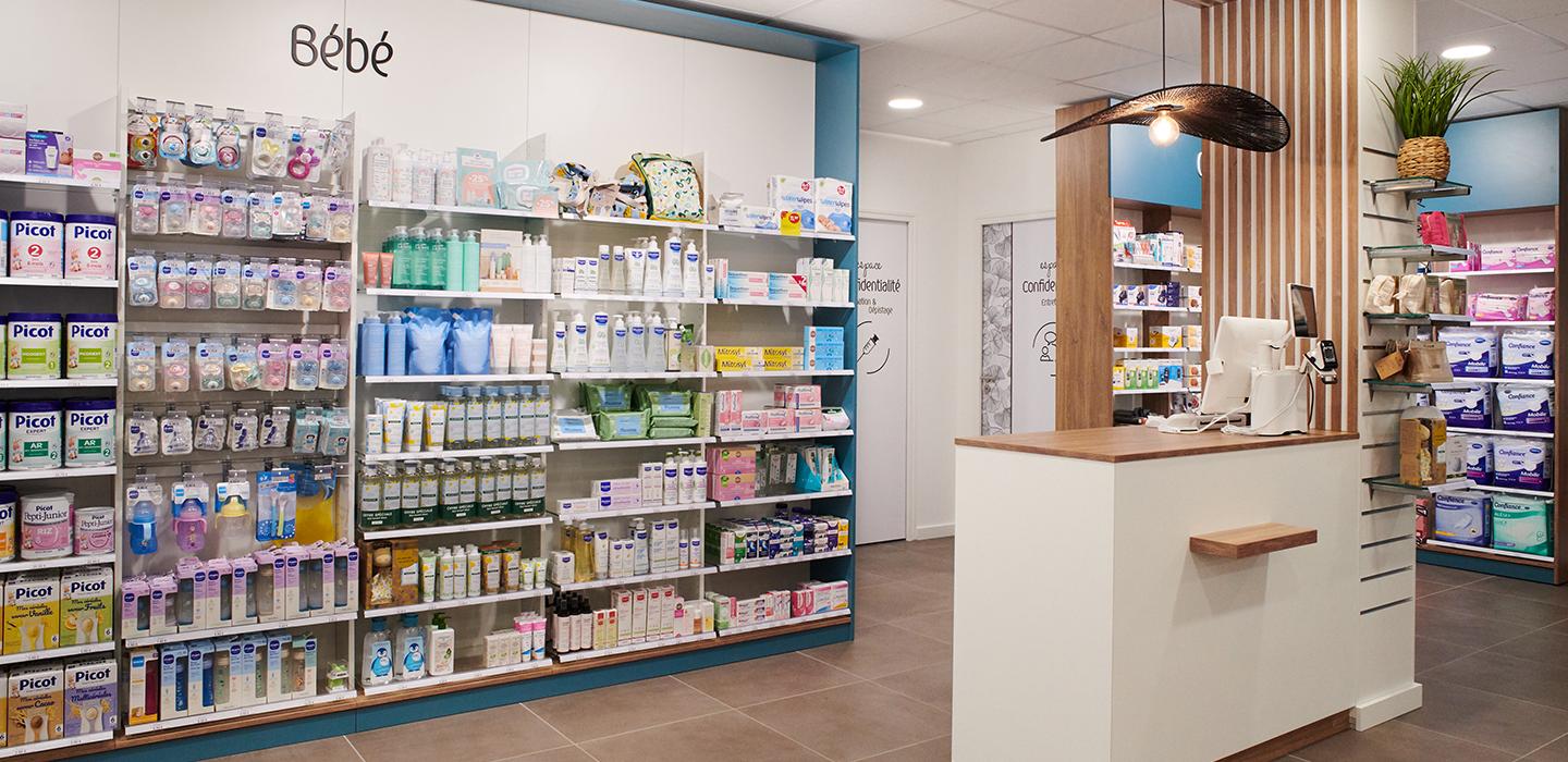 Corner puériculture et univers bébé en pharmacie, encadrement mural bleu et comptoir de retrait rapide sous une retombée de plafond bois.  