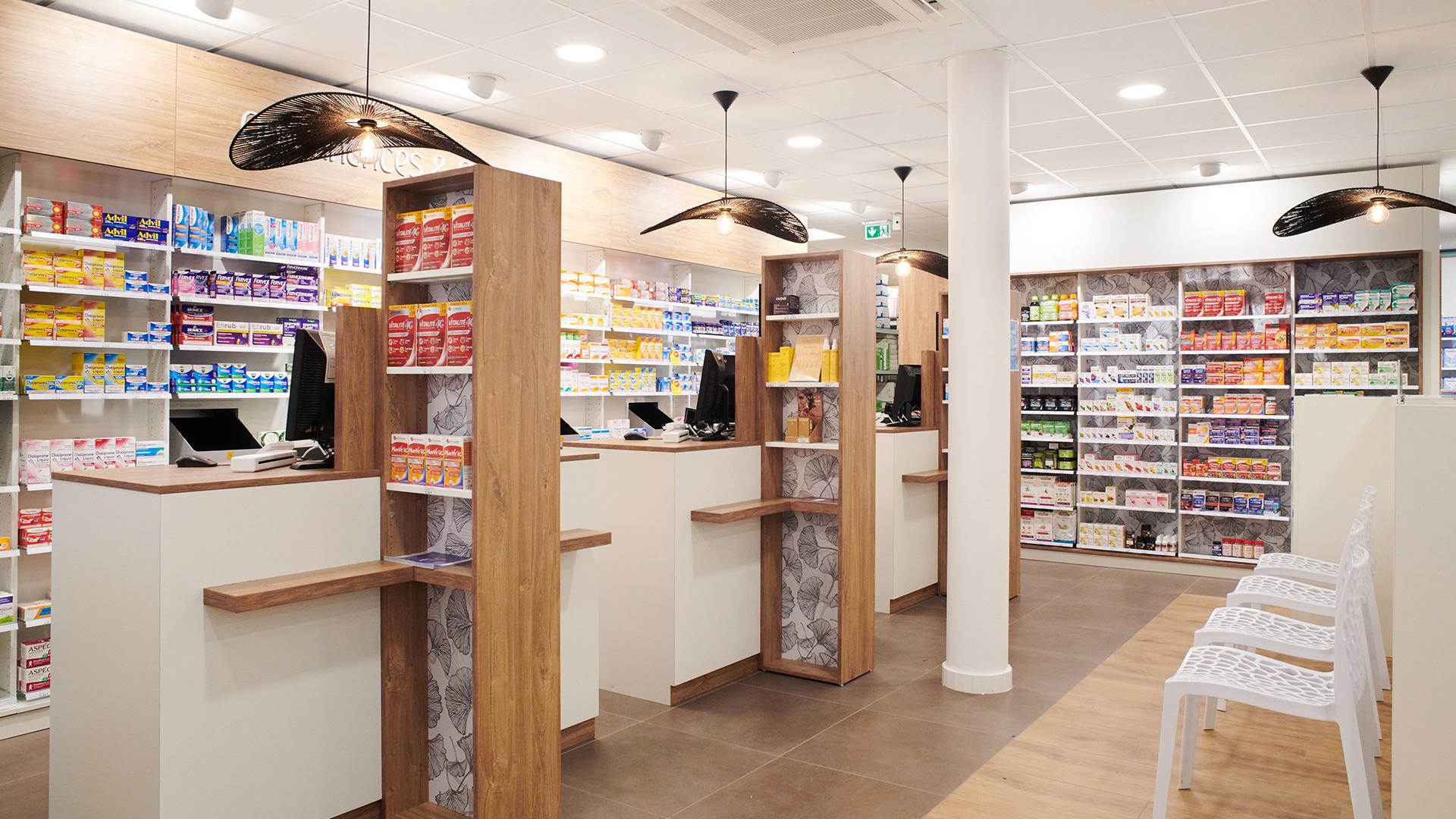 Alignement de comptoirs de pharmacie ergonomiques en bois et blanc, séparations décoratives avec motif Ginkgo et suspensions design noires, agencement signé JBCC