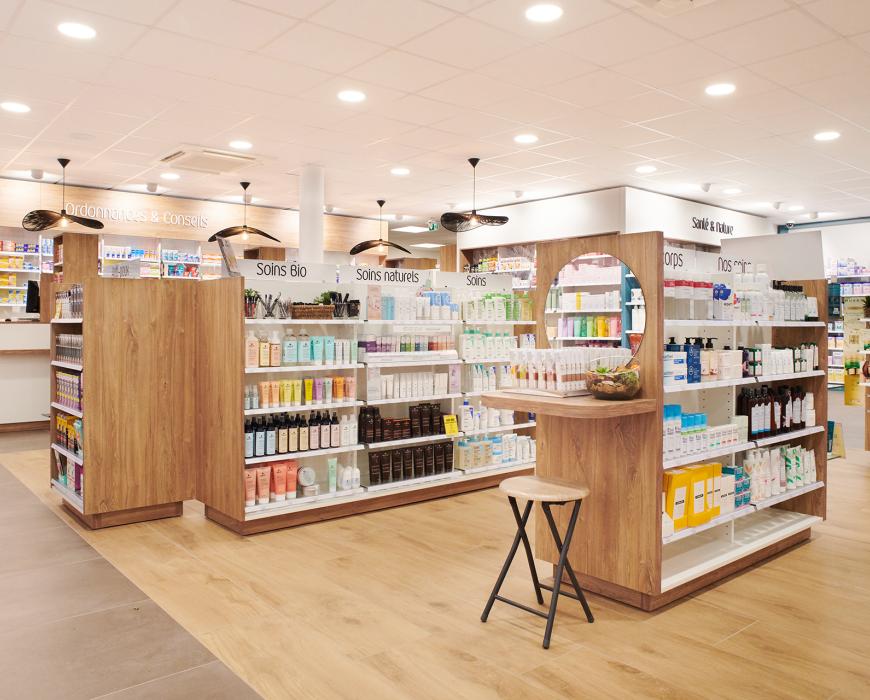 Rayonnages de parapharmacie en bois clair dédiés aux soins naturels et bio, avec gondole centrale équipée d'un miroir, agencement moderne à Machecoul