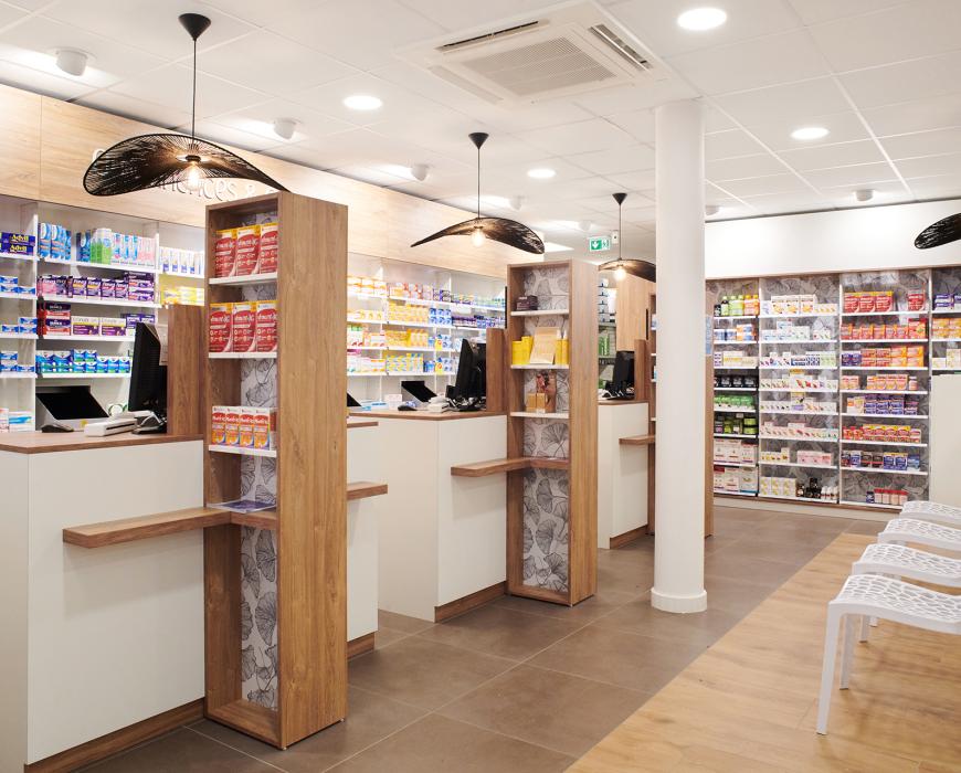 Alignement de comptoirs de pharmacie ergonomiques en bois et blanc, séparations décoratives avec motif Ginkgo et suspensions design noires, agencement signé JBCC