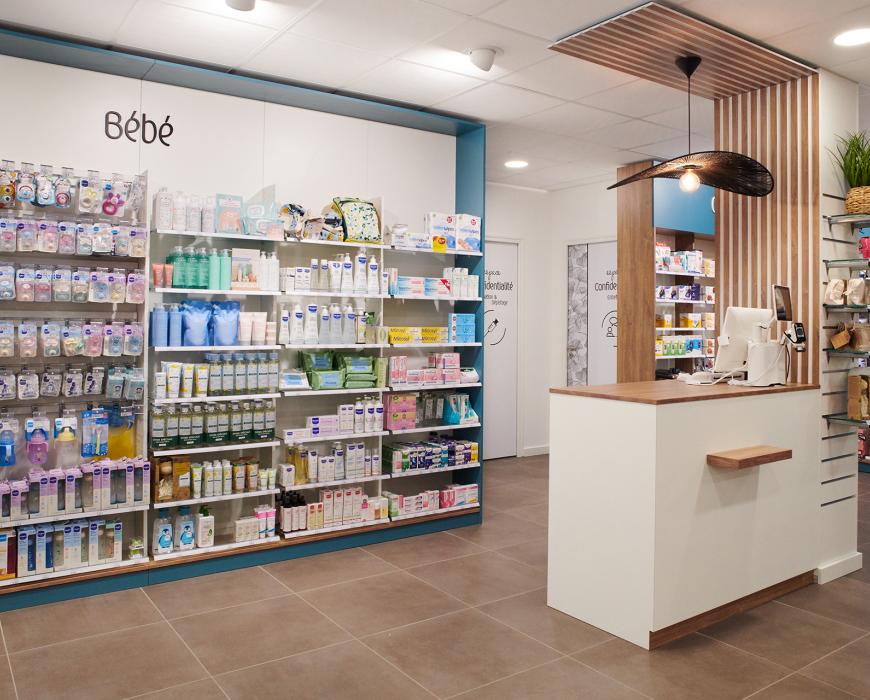Corner puériculture et univers bébé en pharmacie, encadrement mural bleu et comptoir de retrait rapide sous une retombée de plafond bois.  